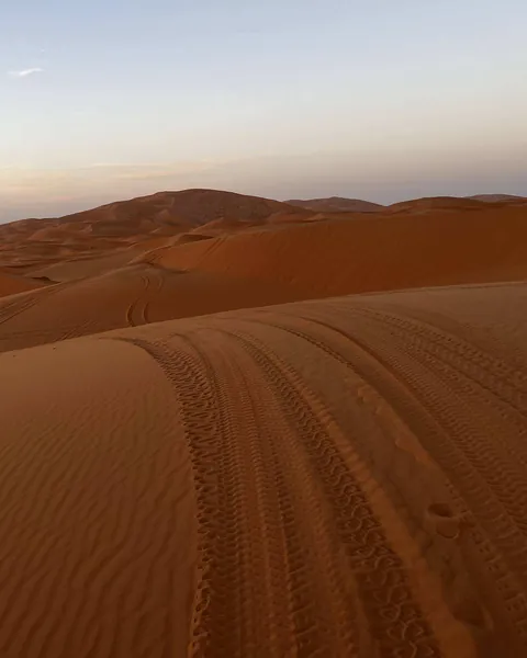 Huellas de neumático sobre la cresta de una duna al atardecer, con el mar de dunas del Erg Chebbi detrás