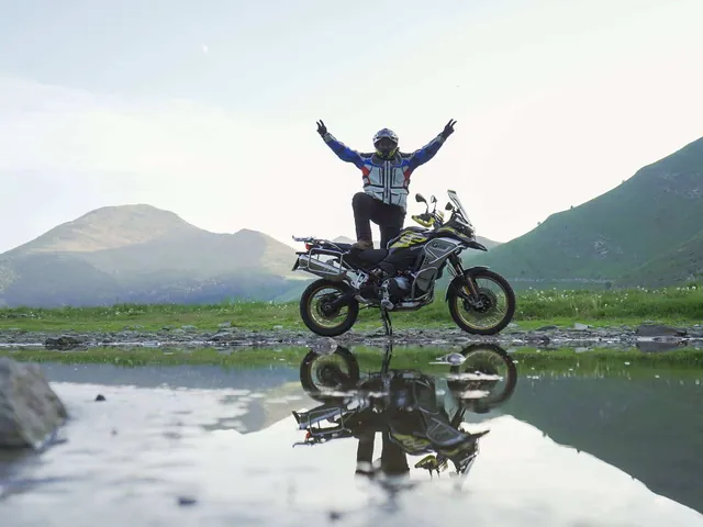 Luis de pie sobre la moto con los brazos abiertos, reflejado en el agua