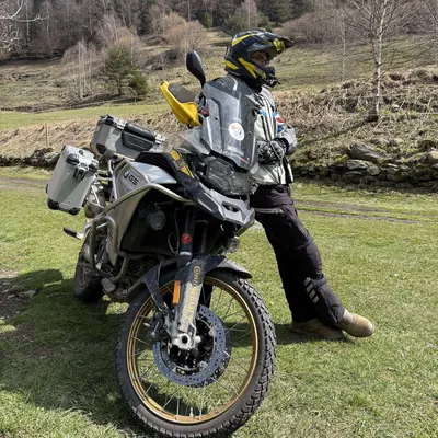 Luis apoyado en su moto trail sobre la hierba, con la montaña detrás