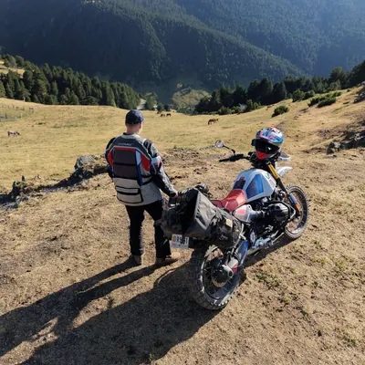 Luis junto a la moto en un prado de montaña, con el valle del Pirineo al fondo