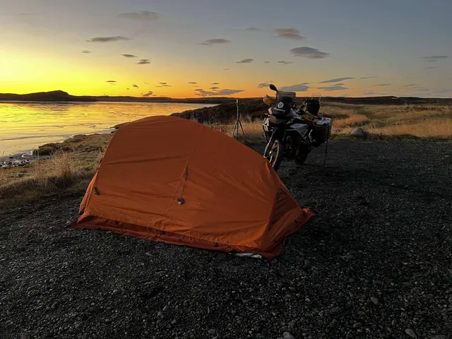 La tienda naranja montada junto a la moto al atardecer