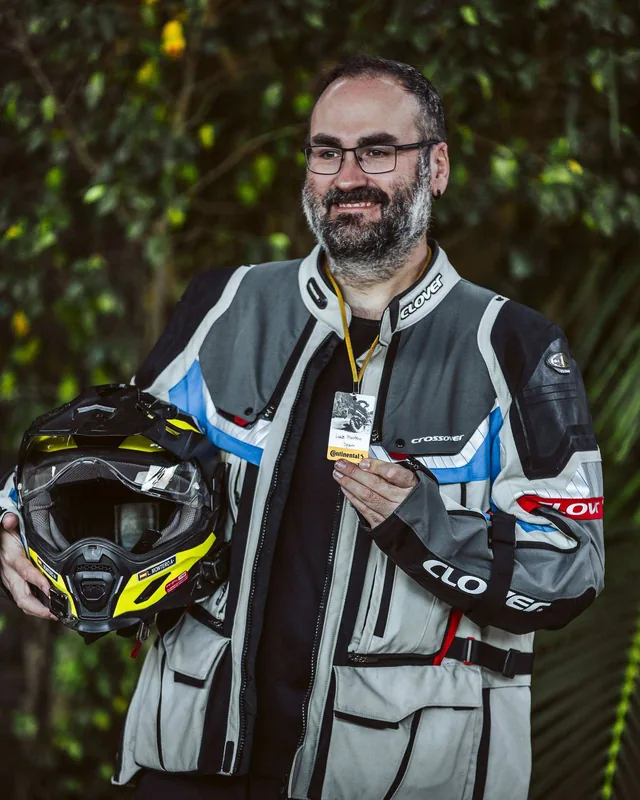 Retrato de Luis sonriendo, con la chaqueta de moto y el casco en la mano