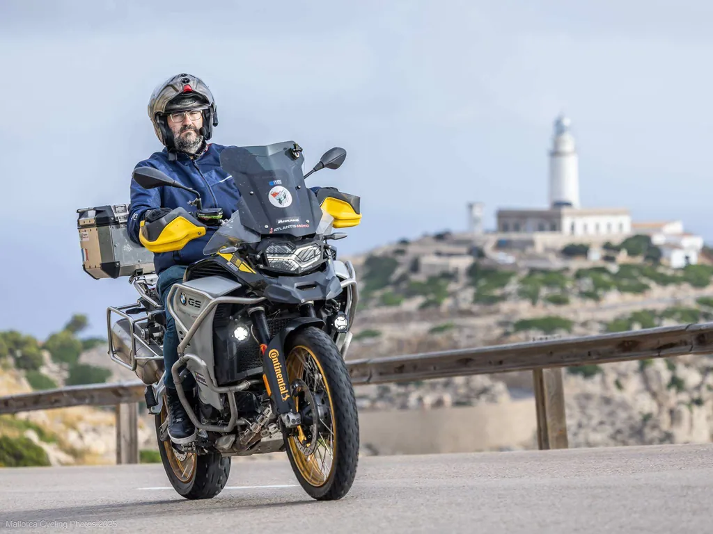 Luis en moto en una curva con el faro de Formentor detrás, en Mallorca