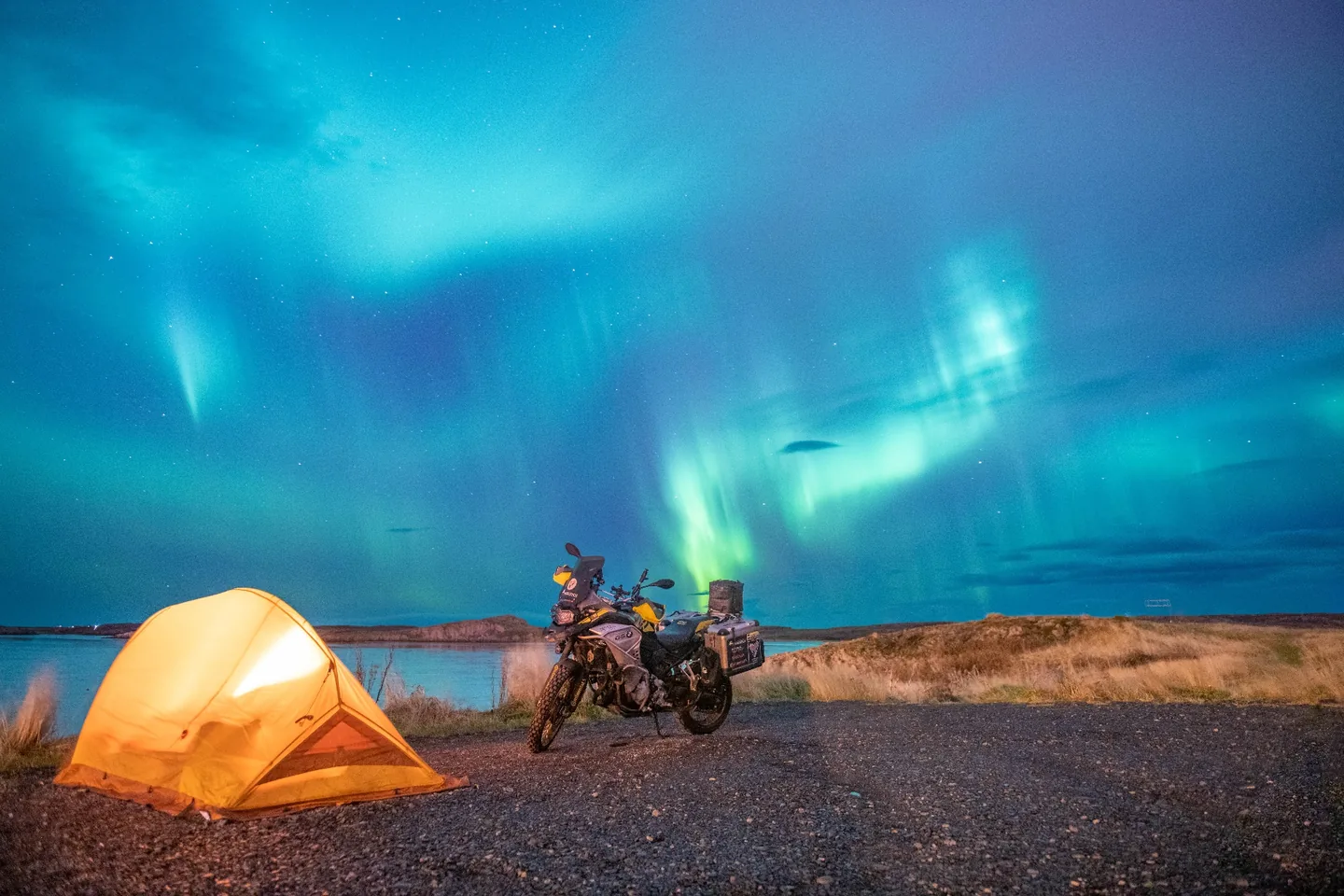 La tienda naranja iluminada y la moto bajo una aurora boreal en Islandia