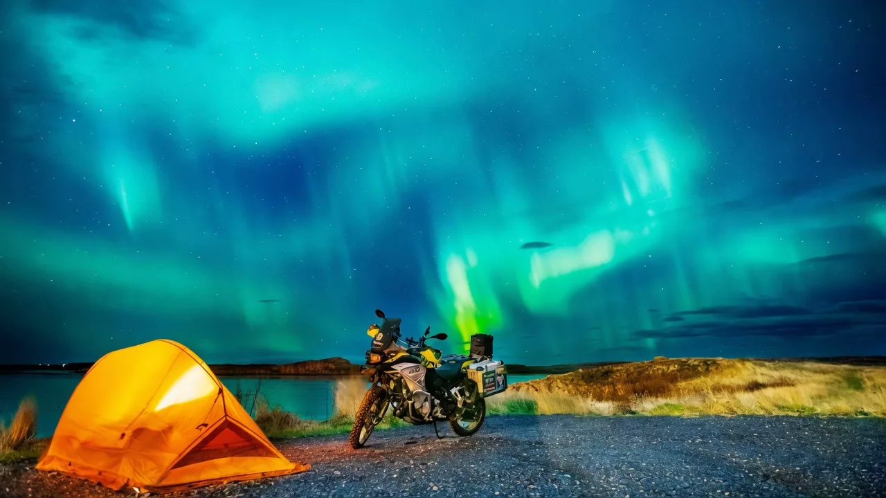 Tienda naranja y moto bajo auroras en Islandia