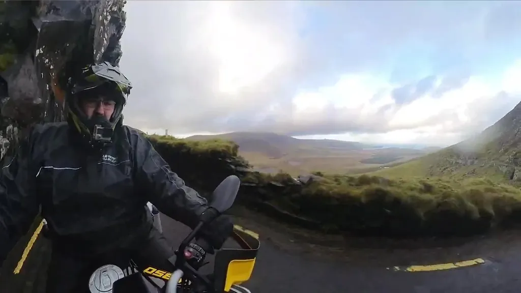 Luis en la moto, con el casco y el traje de agua, en una carretera de montaña con niebla en Irlanda